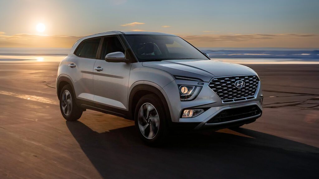 Imagem publicitária para o blog sobre o seguro creta. A imagem mostra um Hyundai Creta 2023 estacionado em uma superfície lisa com um cenário de pôr ou nascer do sol ao fundo. O veículo está posicionado em um ângulo que destaca seu perfil frontal e lateral. Ele possui um design de grade proeminente, faróis elegantes e rodas de liga leve. As condições de iluminação realçam as linhas de design do carro, conferindo-lhe uma estética atraente contra o fundo natural.
