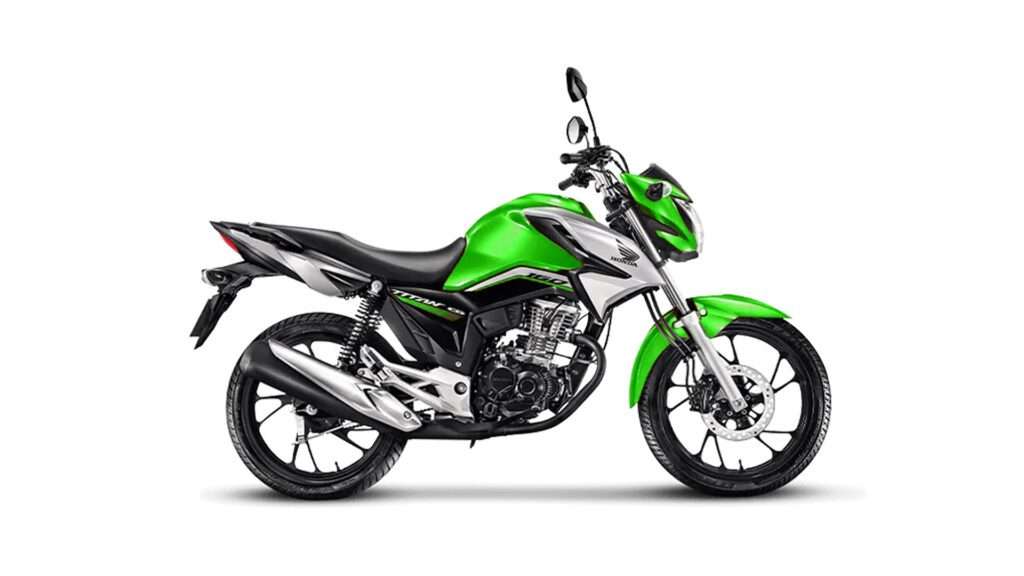 A imagem mostra uma Honda CG 160 verde e preta posicionada à esquerda, contra um fundo branco. A moto parece ser um modelo moderno com características de design esportivo, incluindo linhas e contornos acentuados na carenagem, uma carenagem frontal compacta com farol integrado e rodas com múltiplos raios.