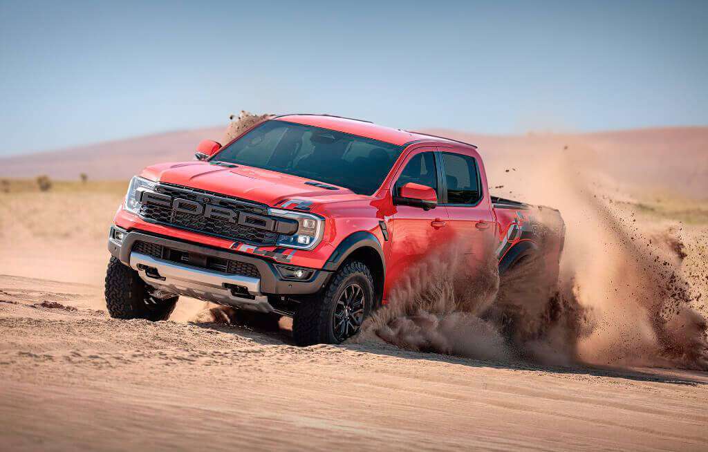 A imagem mostra uma Ford Ranger estacionada em um terreno rochoso com o sol se pondo ao fundo. O veículo está posicionado à esquerda da imagem, capturado em um ângulo lateral-frontal que destaca características como a grade, os faróis e as rodas. O logotipo da Ford é visível na grade frontal e “Ranger” está escrito na parte inferior das portas dianteiras. O pôr do sol proporciona uma luz de fundo quente, criando um contraste interessante com os tons frios da cor do caminhão. Esta imagem parece ser ideal para mostrar o design e o apelo deste modelo específico da Ford Ranger em um cenário ao ar livre, enfatizando suas capacidades como veículo off-road.