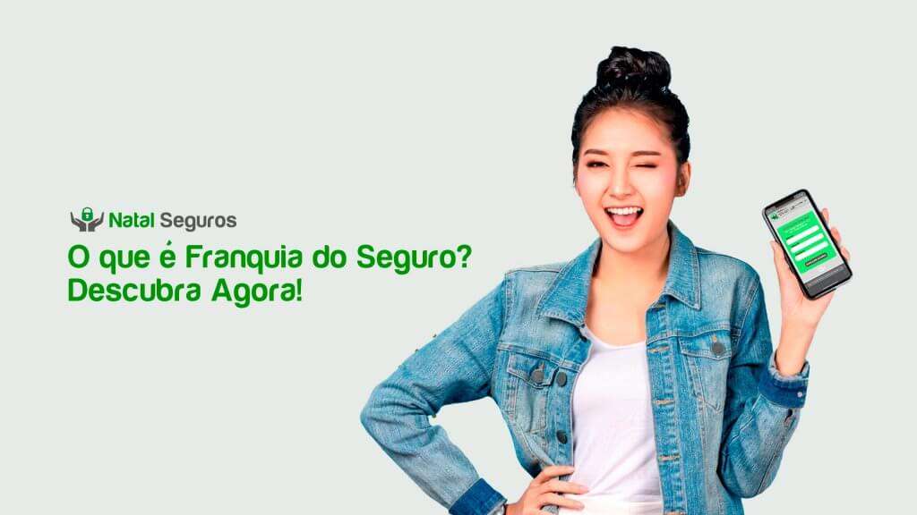 A imagem mostra uma pessoa segurando um smartphone em uma mão e apontando para ele com a outra mão. Ela está vestindo uma jaqueta jeans sobre uma camisa branca. A tela do smartphone exibe uma interface verde com alguns textos e botões. No lado esquerdo da imagem, há um texto em português que diz: "Natal Seguros O que é Franquia do Seguro? Descubra Agora!"