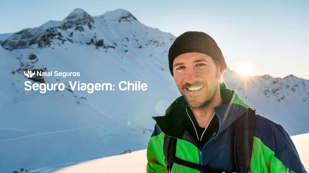 A imagem mostra uma pessoa parada em uma área montanhosa coberta de neve, com o sol se pondo ou nascendo atrás das montanhas. A pessoa está vestindo uma jaqueta verde e azul e um gorro preto. Há um texto na imagem que diz: "Natal Seguros Seguro Viagem: Chile"