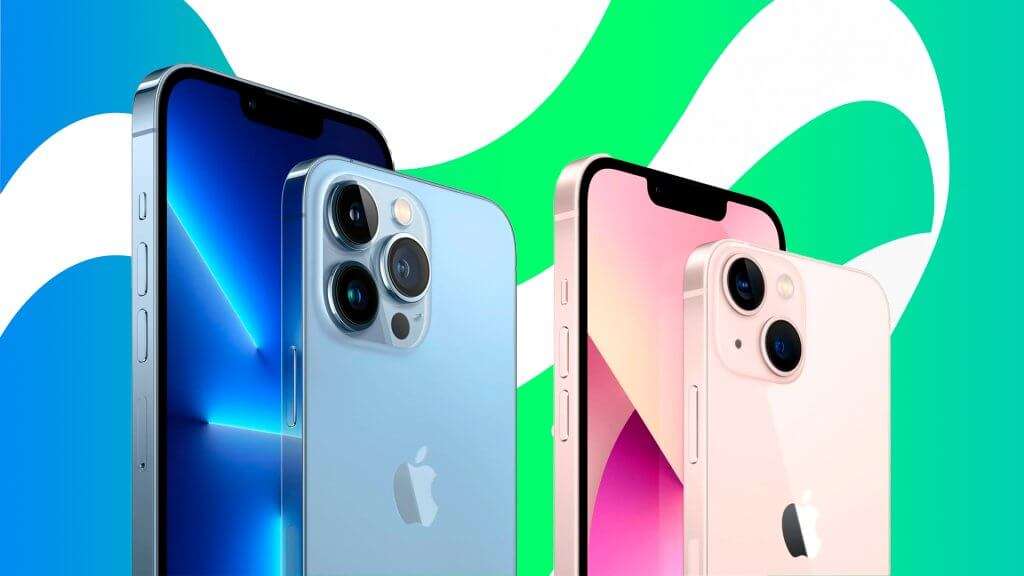 A imagem mostra dois modelos de iPhone 13. O iPhone à esquerda é azul e possui três câmeras traseiras, indicando que é um modelo Pro ou Pro Max. O iPhone à direita é rosa e possui duas câmeras traseiras, sugerindo que é um modelo padrão ou Mini. Ambos os telefones têm o logotipo da Apple na parte traseira e estão posicionados em um fundo com cores verde e azul.